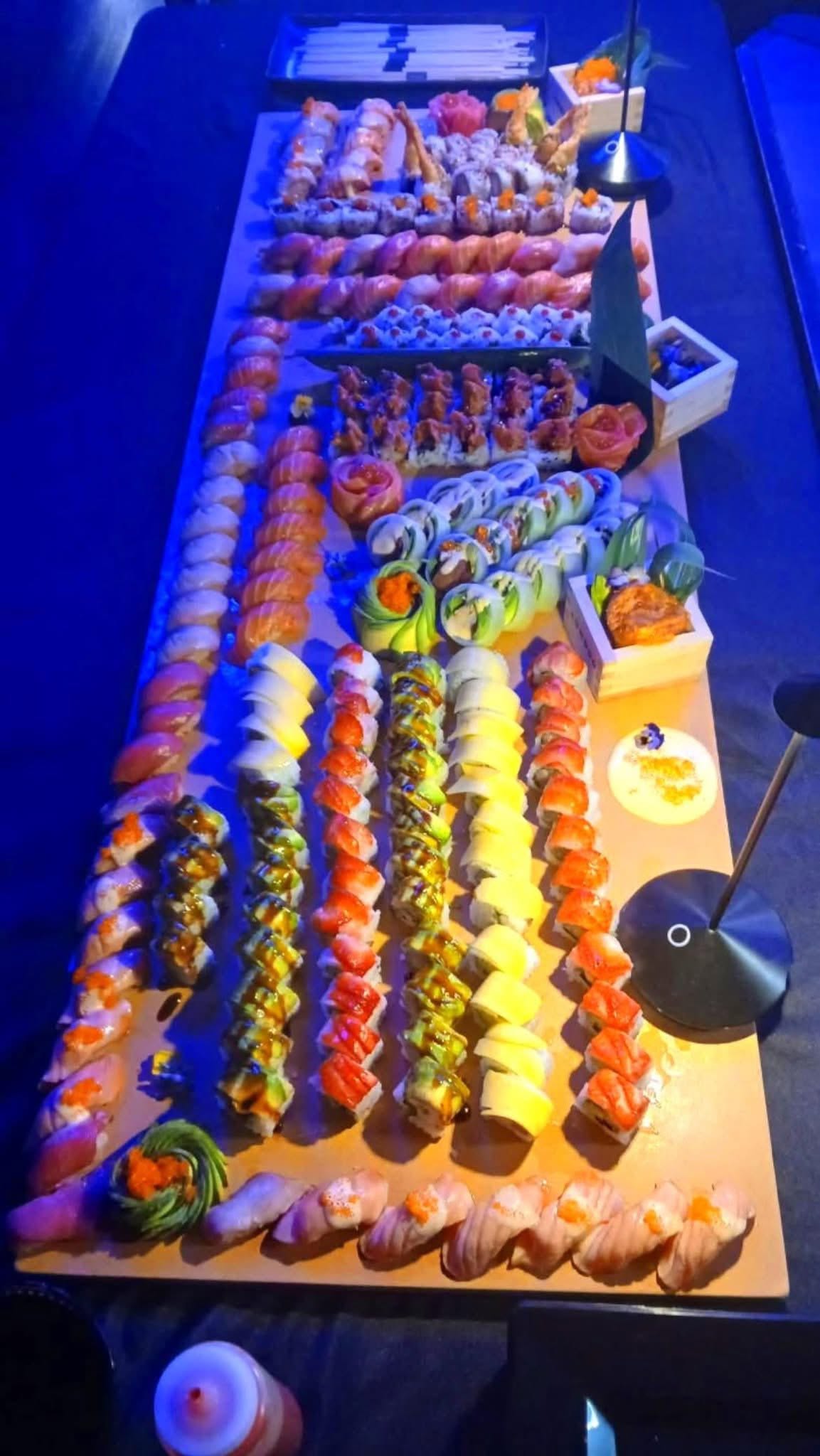 Massive catering sushi spread with dozens of rolls and nigiri under blue lighting